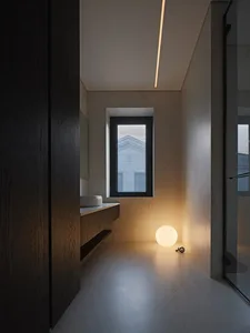 Modern minimalist bathroom with marble finishes, featuring a single window and warm, ambient lighting.