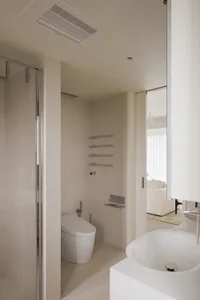 Modern minimalist bathroom featuring a white tiled floor and walls, with a sleek white toilet and matching sink.