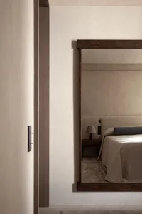 A minimalist bedroom with a bed covered in neutral-toned textiles and a mirror on the wall.