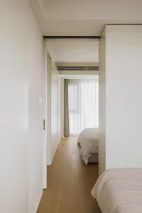 Minimalist bedroom featuring white walls and floor, with a bed and curtains.