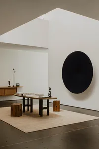 An interior space featuring wood and metal furniture, a black circular wall art, and a low table with books and objects.