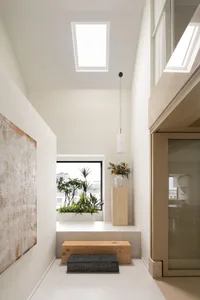 A minimalist interior space featuring white walls, a wooden bench, and glass windows.