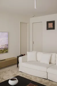 A minimalist living room with a white canvas couch, wooden flooring, and white walls.