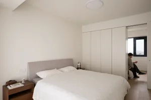 Minimalist white bedroom with a large bed, white bedding, and neutral-colored walls and closet doors.