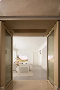 A modern living room with light brown material walls, white furniture, and a large artwork.