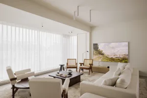 A modern minimalist living room featuring a couch, chairs, and a coffee table with a painting and windows with sheer curtains