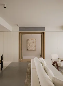 A minimalist modern living room with neutral tones, featuring a white sofa, white armchair, and a beige abstract painting on