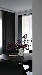 A minimalist interior design featuring a white ceramic vase with dark leaves on a black wooden table.