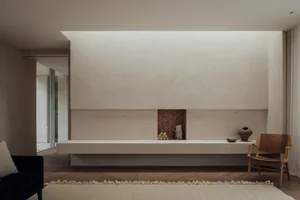 Modern minimalist living room with a concrete fireplace, wooden floor, and a few pieces of furniture.