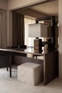 A modern desk space featuring a wooden desk with a lamp and a stool.