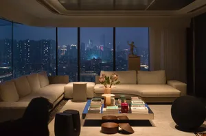 A modern living room with cityscape view, featuring a beige sectional sofa, coffee table, and decorative items.