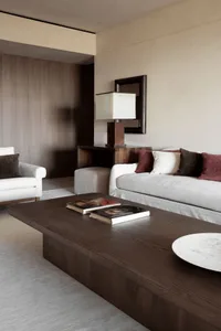 A modern living room featuring a wooden coffee table, white and red cushions, and a white armchair.