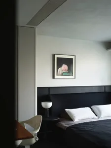 A minimalist bedroom featuring black furniture, a white chair, and a framed picture on the wall.