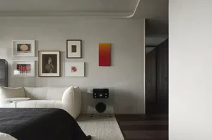 Neutral-colored bedroom with minimalist design, featuring a white sofa and a single orange-red abstract painting.