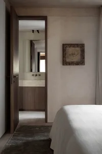 Minimalist bedroom with neutral tones, featuring a bed, a door leading to an en-suite bathroom, and a framed artwork on the w