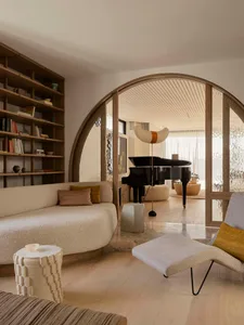A minimalist living room featuring beige and brown furniture, a grand piano, and a curved wall.