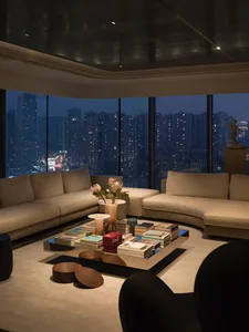 A modern minimalist living room with beige sofas, a square coffee table with books and decorative items, and a cityscape view
