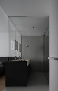 A minimalist modern bathroom with concrete walls and floor, featuring sleek black cabinetry and a long sink counter.