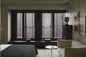 Modern bedroom featuring metal blinds, a textile bed, a sofa, a lamp, and decorative pictures.