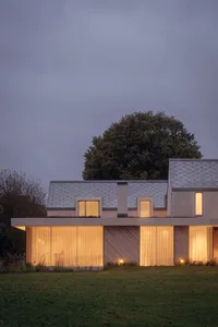 Modern house with glass exterior at dusk, highlighting the sleek design and warm indoor lighting.