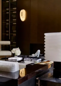 A modern interior design featuring a glass side table with books, flowers, and a tiger figurine.