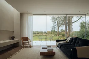 Modern living room with a glass wall overlooking a serene outdoor landscape.