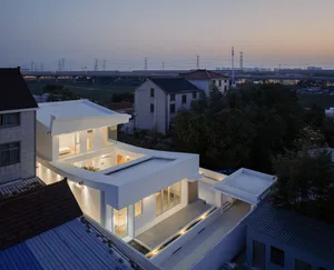 An aerial view of a modern residential building illuminated at dusk, featuring sleek white exterior and large windows.