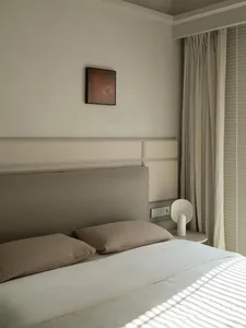 A minimalist bedroom with a bed, pillows, and a side table with a lamp.