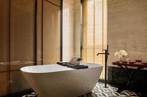A minimalist bathroom with a freestanding bathtub, marble walls, and a window with blinds.