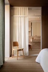 A minimalist bedroom featuring wooden furniture and a white bed.