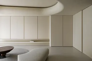 Modern minimalist living room with concrete walls and floor, featuring a curved ceiling and a single wooden table.