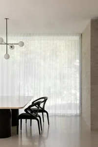 Minimalist modern dining room with concrete table and black chairs behind sheer curtains.