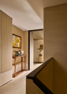 A modern corridor with wooden paneling, leading to a hallway adorned with artwork and decorative plants.