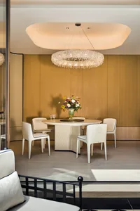 A modern dining room with a white marble table, white chairs, and a flower arrangement on the table.