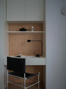 A minimalist study desk with a wooden background, metal frame, and black chair.