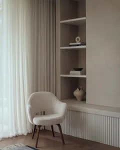 A minimalist interior space with a white plush chair and built-in shelves.