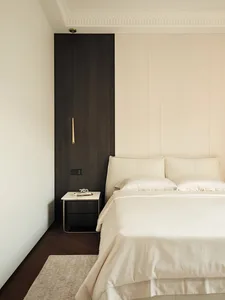 A minimalist bedroom with a white bed, beige bedding, and a dark wooden headboard.