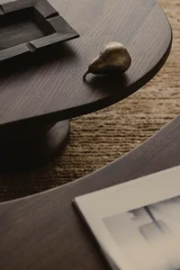 A bronze pear-shaped decorative object placed on a wooden curved table, featuring textured surface and modern design aestheti