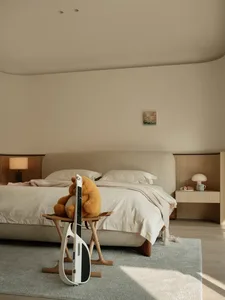 A minimalist bedroom with a beige upholstered bed, wooden nightstands, and a light blue rug.