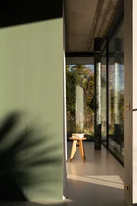 A minimalist interior with concrete walls and glass elements, featuring a small wooden stool with books on it.