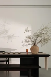 極簡室內設計，木桌上擺放花瓶與小杯，置於桌墊之上。