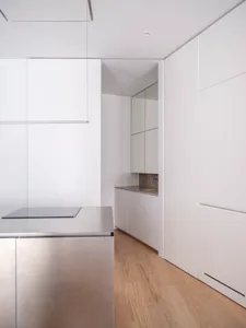 Modern minimalist kitchen with white surfaces and stainless steel appliances.
