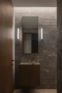 A modern bathroom with stone tiles, a floating vanity, and a rectangular mirror with LED lighting on either side.