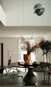 Modern dining room with white marble pedestal table, glass vase with dried plants, transparent acrylic chairs, and large glas
