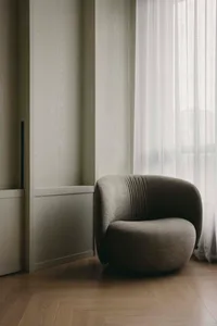 A modern living room featuring a textured fabric chair next to a window with sheer curtains.