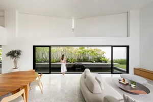 A modern living room with white concrete walls and floor, large sliding doors, and a serene outdoor garden view.