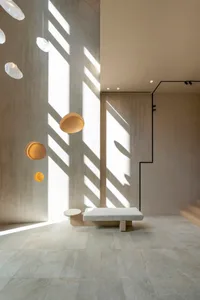 A minimalist interior space featuring exposed concrete walls, a white bench, and floating circular lights.