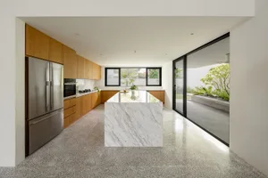 Modern minimalist kitchen featuring marble countertops, wood cabinetry, and a terrazzo floor.