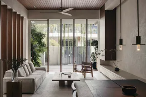 A modern minimalist living room with large windows, a wooden floor, concrete wall, and plants.