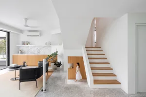 A modern residential interior featuring a staircase with white marble and wooden steps, white walls, and wooden cabinetry.